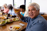 Portrait of multiracial senior man enjoying wine while having lunch with friends at dining table