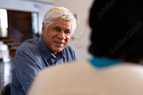 Smiling biracial senior man talking with female friend while sitting for lunch in nursing home