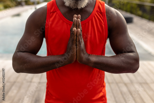 Midsection of african american senior man meditating in prayer position while standing in yard