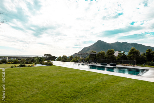 Scenic view of grassy land and swimming pool against mountain and cloudy sky
