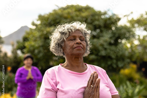 African american senior woman with eyes closed meditating against trees in yard at nursing home