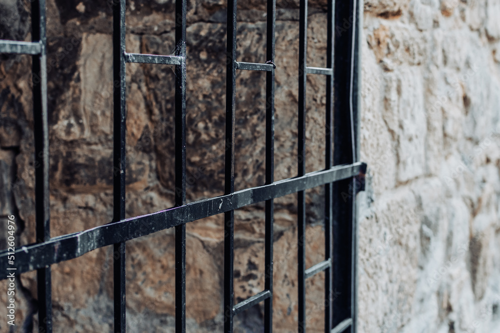 Old medieval prison gate made of black bars and wall made of rocks shot in perspective Old medieval prison gate made of black bars and wall made of rocks shot in perspective