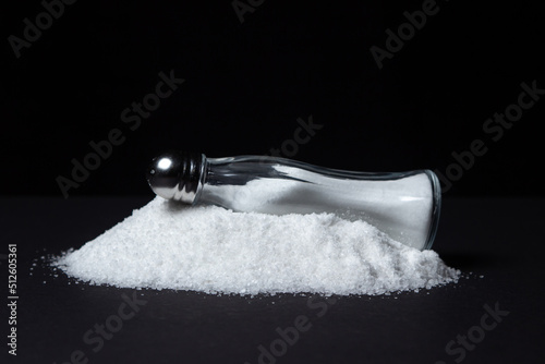 Salt shaker on a pile of salt on a black background. Excessive salt intake. food salt