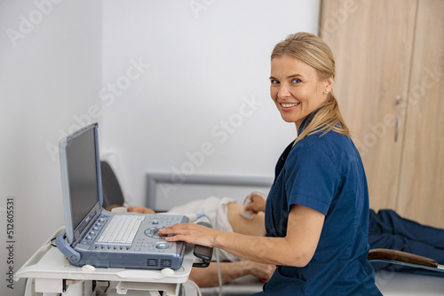 Smiling doctor ultrasound examine senior patient abdomen at hospital and looking camera photo