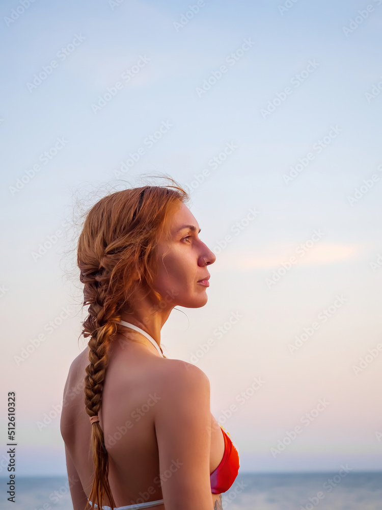 Portrait of a fair-haired girl in a bikini standing on the background of the sea on a summer day. Profile view Portrait of a fair-haired girl in a bikini standing on the background of the sea on a summer day. Profile view