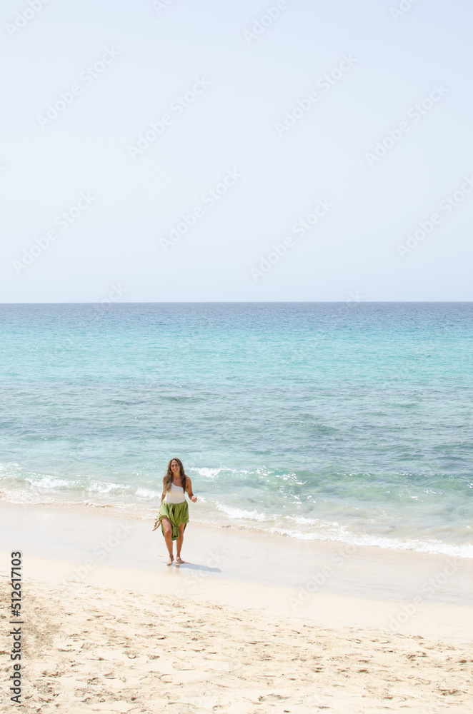 beautiful middle-aged woman walking on the beach. she feels happy, strong and free. dressed woman tourist stands alone on the beach in the canary islands. beautiful middle-aged woman walking on the beach. she feels happy, strong and free. dressed woman tourist stands alone on the beach in the canary islands.