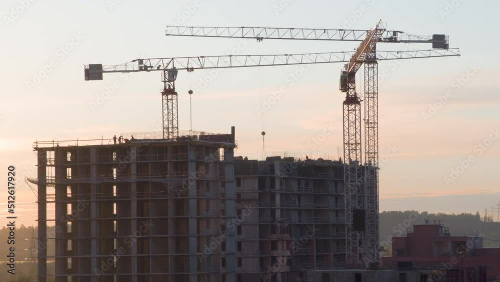Construction of a Residential Building. Time-Lapse. Three tower cranes tower over a residential complex under construction. Intense work in progress against the background of the evening sky Construction of a Residential Building. Time-Lapse. Three tower cranes tower over a residential complex under construction. Intense work in progress against the background of the evening sky
