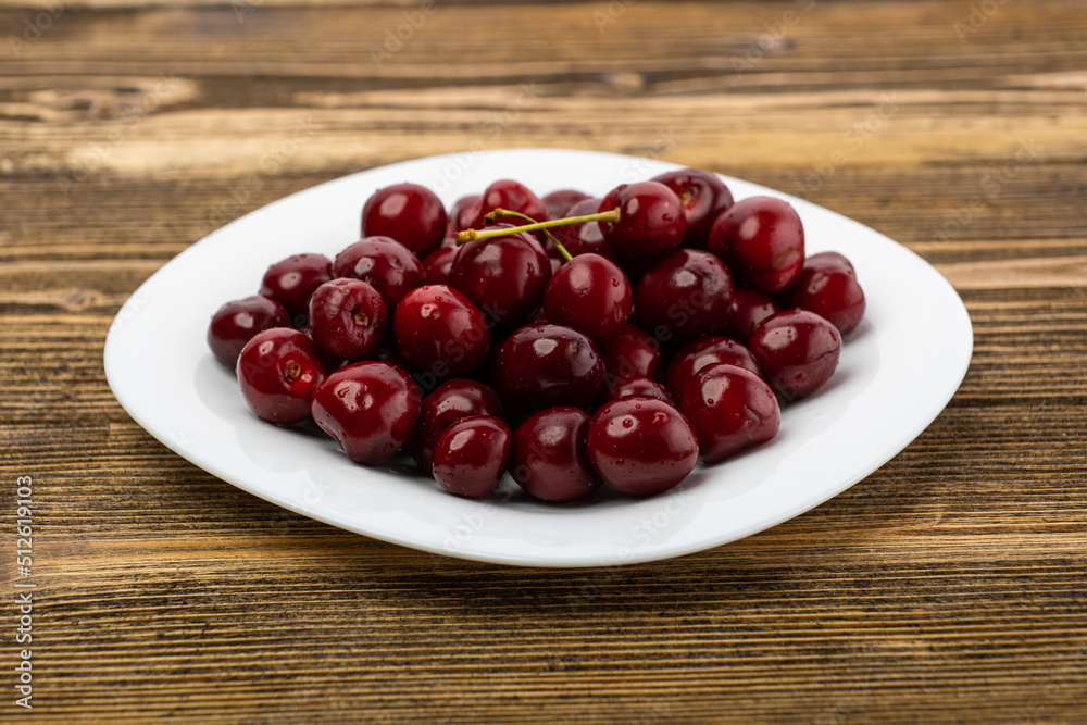 ripe red cherries in a white plate on a wooden background ripe red cherries in a white plate on a wooden background