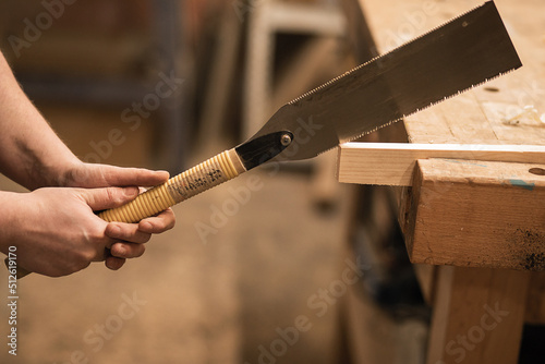 Unrecognizable male carpenter hands sawing and using chisel or rasp with plank timber on workbench. Furniture production