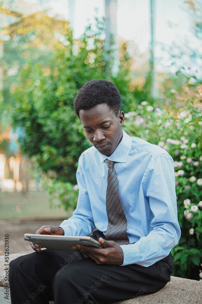 African businessman using a tablet computer while he is sitting on a bench African businessman using a tablet computer while he is sitting on a bench