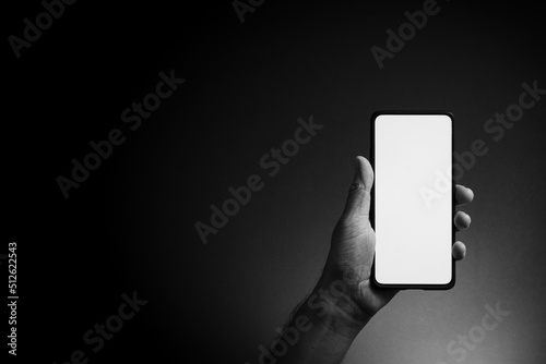 Man's hand holding smartphone with blank screen isolated on dark background
