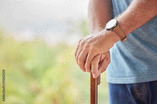 Senior disabled man hands holding a cane outside in a nursing home park. Closeup of elderly male holding a walking aid outdoors, relaxing at a healthcare facility on the sunny day