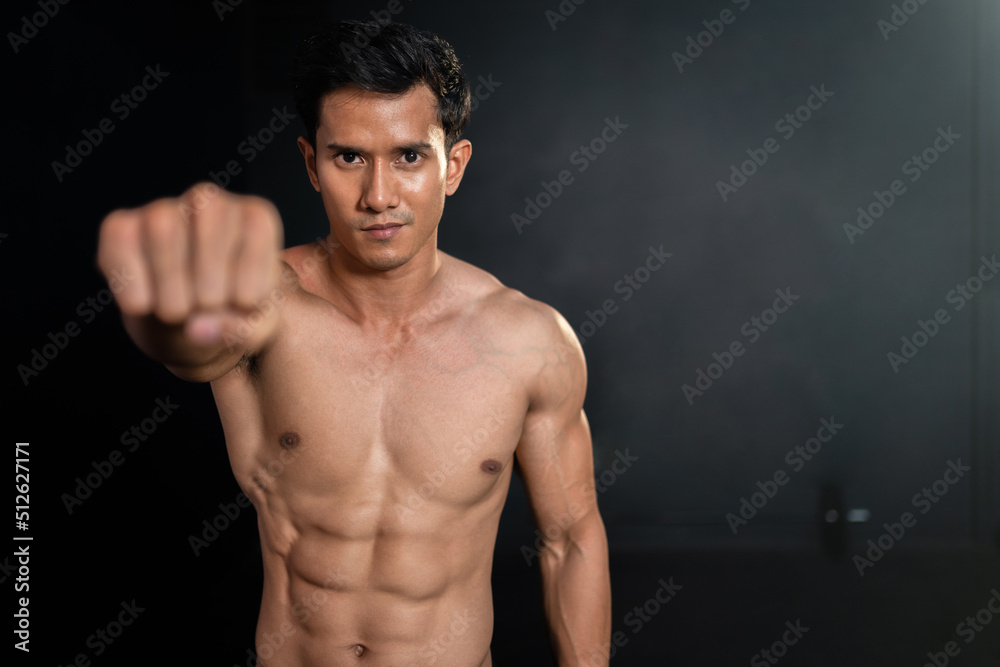 Asian strong muscular man clench fist showing six pack on black background in fitness gym.Sportsman workout powerful at sport club.
