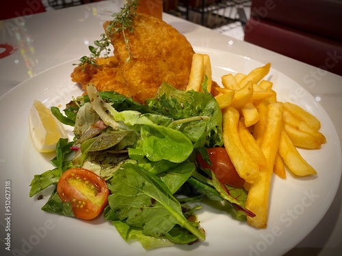 A Plate of fish and chips with battered fish, potato chips, fresh salad, tartar sauce, French fries and lemon wedge with blurry noise background