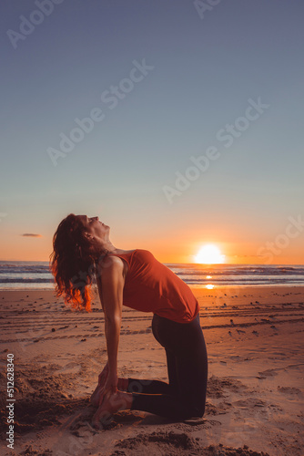 woman doing yoga on the sand of the beach at sunset while the sun sets over the sea