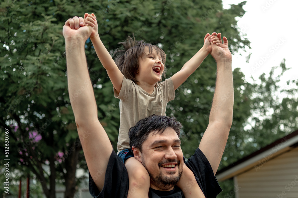 a happy, laughing baby sits on dad's shoulders, they dance and have fun. A father spends time with his son. The concept of a happy family

