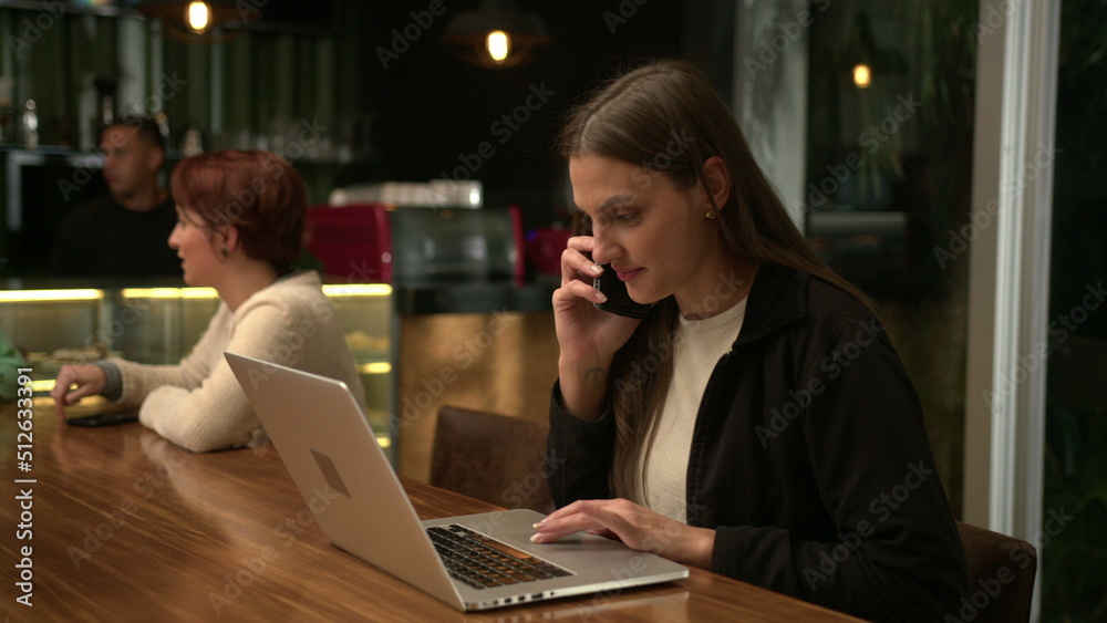 People inside coffee shop at night. Young millennial woman browsing internet online sitting at cafe
