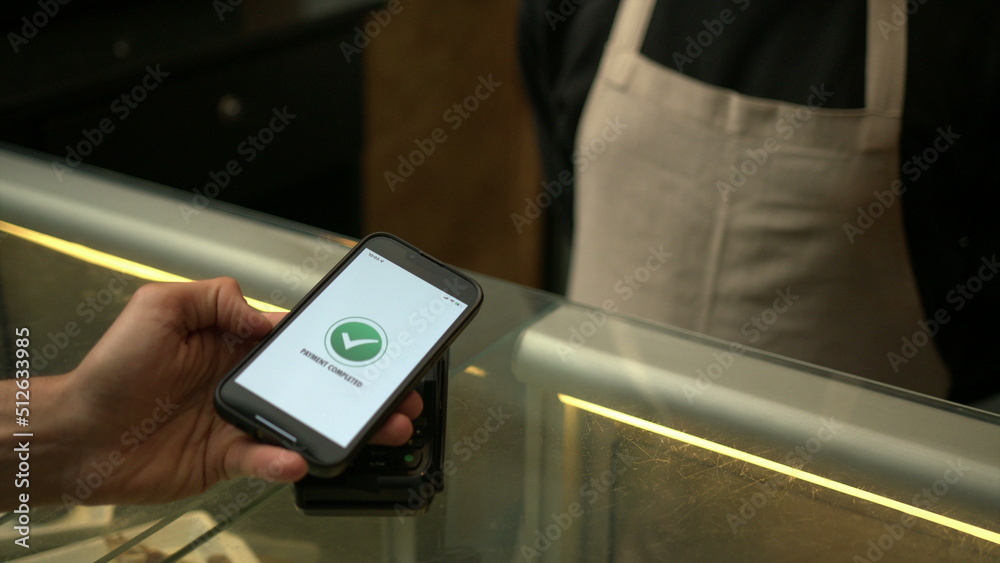 Customer paying with contactless NFC payment technology on smartphone device inside business store