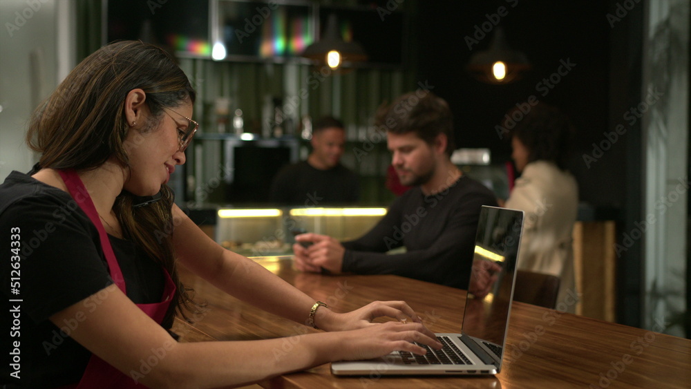 Barista receiving orders on phone browsing online with laptop at cafe. Small business concept of staff using computer at coffee shop Barista receiving orders on phone browsing online with laptop at cafe. Small business concept of staff using computer at coffee shop
