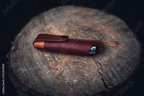 A folding knife with a handmade leather sheath on a log. photo