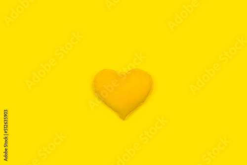 Un corazón amarillo de tela hecho a mano sobre un fondo amarillo liso y aislado. Vista superior y de cerca. Copy space