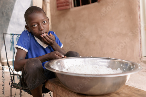 Poor African boy eating plain rice without seasoning, vegetables or meat froma big metal bowl; malnutrition concept photo