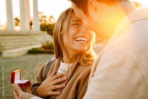 White man smiling and proposing to his girlfriend in park photo