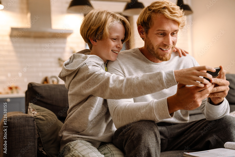 Obraz premium Ginger man using mobile phone while making fun with his son