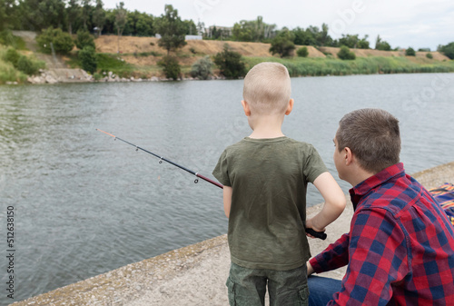 Father and son fishing. Dad shows his son how to hold the spinning and spin the reel. Fishing training on a pond or river. Caring parent concept.