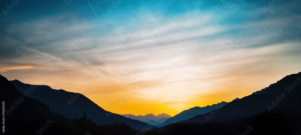 Mountain landscape panorama background - Sunrise or sunset with silhouette of mountains alps and orange sky..