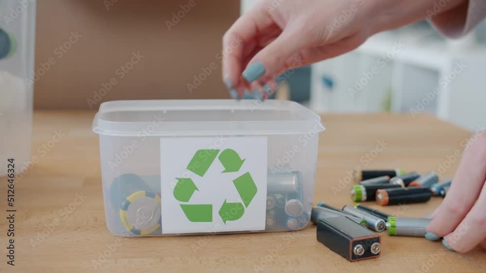 Female hands putting old used batteries in container with recycling symbol indoors at home. Hazardous waste and taking care of environment concept.