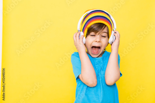 Handsome little boy in blue shirt and colorful hat with headphones, yellow background, banner