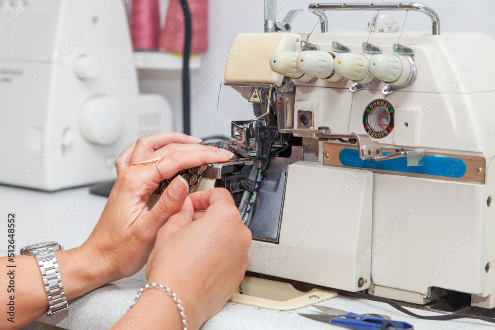 Beautiful young woman designer is working on an overlock machine. Hands close up