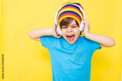 Handsome little boy in blue shirt and colorful hat with headphones, yellow background, banner