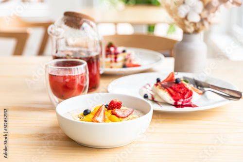 Concept of healthy breakfast in cafe with kinfolk style interior. Breakfast with herbal tea  oatmeal porridge  cottage cheese fritters and pancakes with berry sauce.