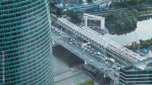 Top view of high-rise and traffic on bridge. Action. View from high-rise building of part of neighboring office skyscraper and bridge with cars. Traffic in business center of city