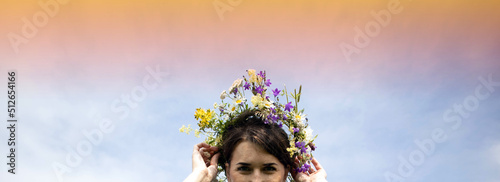 A pretty girl holds a wreath of flowers with her hands. Summer solstice concept. Place for text