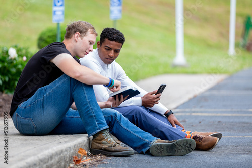 Two men sitting on sidewalk looking at the Bible