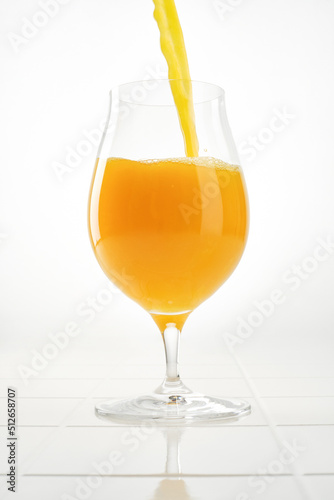 Orange juice pouring into drinking glass on white background. Shallow depth of field