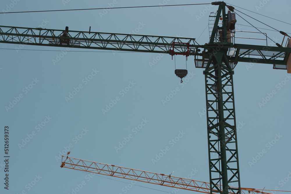 Construction cranes against blue sky view from below. Construction site. Tower crane or slewing crane. Housing business concept. Building modern houses. Engineering lifting equipment. Real estate. Construction cranes against blue sky view from below. Construction site. Tower crane or slewing crane. Housing business concept. Building modern houses. Engineering lifting equipment. Real estate.