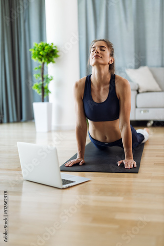 Young woman watching online fitness class while doing stretching exercises at home