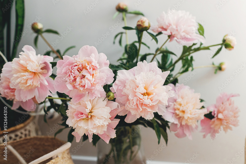Fototapeta premium Beautiful peonies bouquet in modern boho room. Gentle pink peony flowers in vase on rustic background, moody image. Modern bohemian decor, stylish comfy interior details