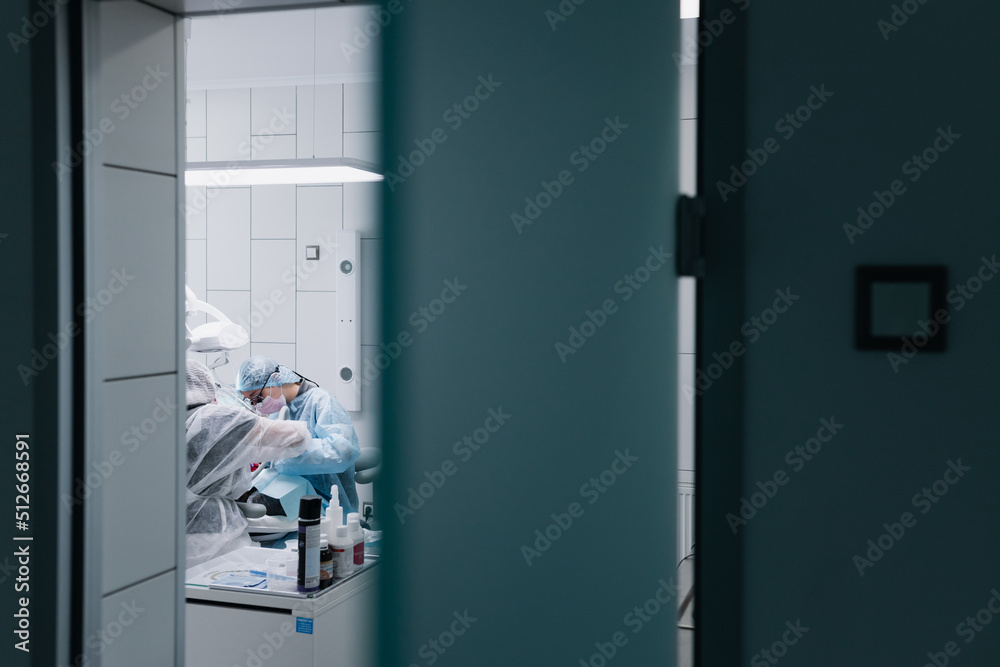 The process of preparing and cleaning teeth. A female professional dentist and an assistant are working. Photo through the door The process of preparing and cleaning teeth. A female professional dentist and an assistant are working. Photo through the door