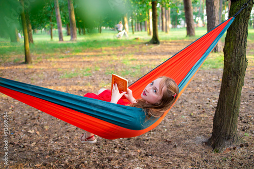 Smiling woman reading a book, relaxing on the hammock in forest, leisure time and summer holiday concept