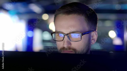 Close up view of a focused man with glasses in front of a computer.