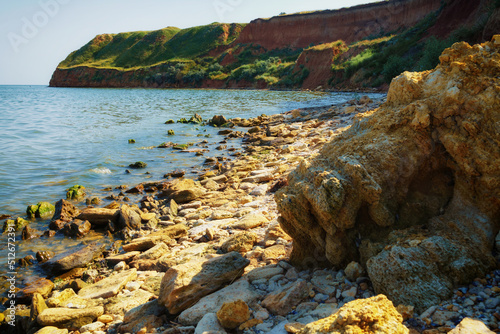 beautiful summer seascape, seashore on a bright day, high hill, wild grass and stones photo