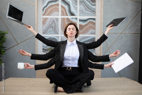 Canvas Print Young business woman with many hands sitting on the desk and meditating, she holds documents, laptop and a cup of coffee