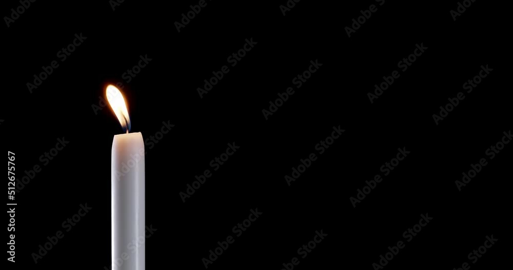 A single white candle burning.Isolated candle burning with dark background.White paraffin candle with yellow shades burns on a black background.Background or illustration of remembrance or celebration