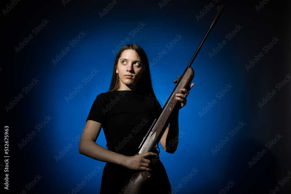 young beautiful woman with long hair in a black t-shirt holding a gun on a blue background young beautiful woman with long hair in a black t-shirt holding a gun on a blue background