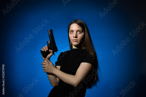 young beautiful woman with long hair in a black t-shirt with a gun on a blue background